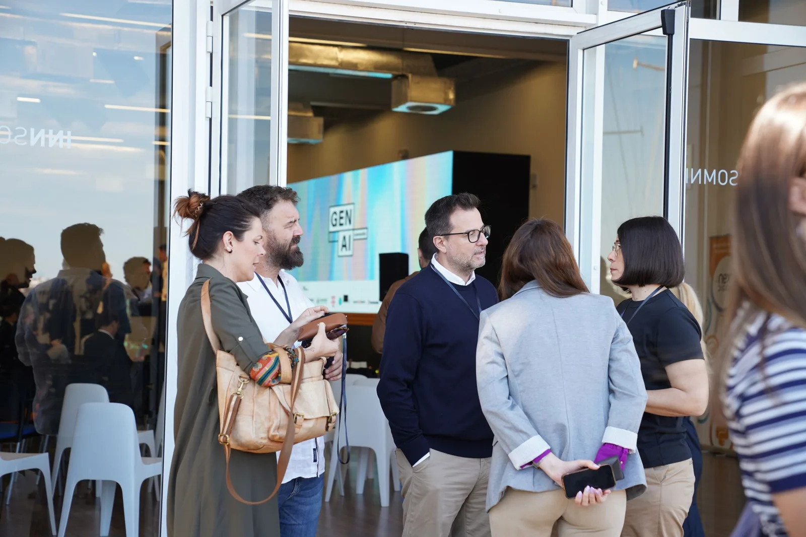 Asistentes conversando en la entrada del venue del Gen AI Summit EU 2026, con la pantalla del evento de fondo